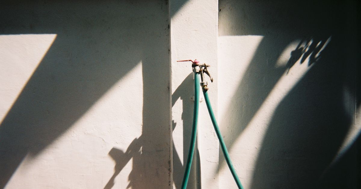 Water tap with hose casting distinct shadows on a wall in daylight.