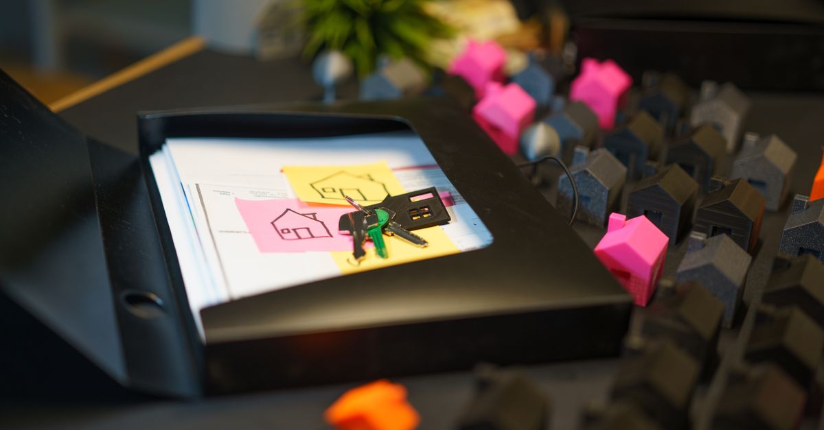Keys and real estate documents on a desk surrounded by colorful house models, symbolizing property transactions.