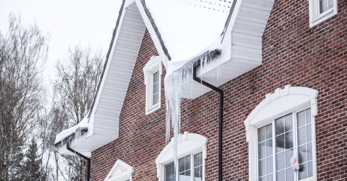 A brick house with snow-covered roof and icicles in a winter setting.